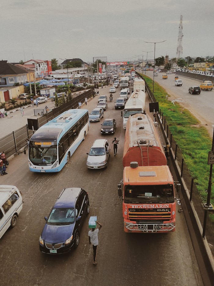 A bustling urban road with diverse vehicles including buses, cars, and trucks during the day.